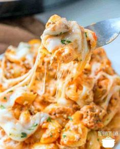 a fork full of cheesy pasta with meat and cheese on it is being lifted from the casserole dish