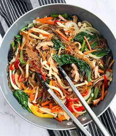 stir fried vegetables in a wok with tongs on a marble counter top, ready to be eaten