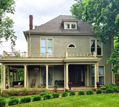 a large gray house sitting on top of a lush green field with lots of trees