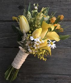 a bouquet of yellow and white flowers on a wooden surface with greenery in the foreground