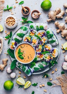 an assortment of vegetables and dipping sauce on a white plate surrounded by garlic, limes, ginger, peanuts