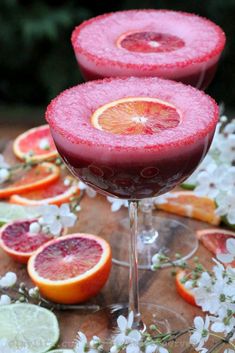 two glasses filled with blood orange margaritas and garnished with fresh flowers on the side