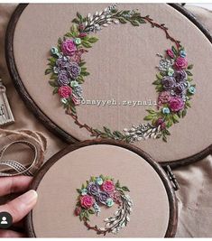 two hand embroidered hoops with flowers and leaves on them, one is holding a ring