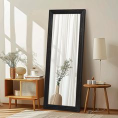 a large black framed mirror sitting on top of a wooden floor next to a table