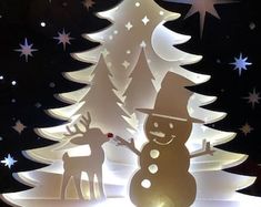 a paper cut snowman and reindeer in front of a lit christmas tree with stars