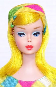 a close up of a doll with blonde hair and blue eyes wearing a multicolored dress