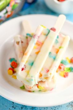 three popsicles on a white plate with gummy bears in the background and candy candies all around them