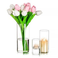 a vase filled with white and pink tulips next to two candles