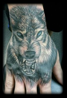 a person's hand with a wolf tattoo on it and an evil looking face