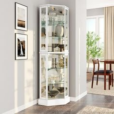 a tall white curio cabinet with glass doors in a living room area next to a dining room table