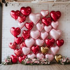 many heart shaped balloons are arranged on the wall in front of flowers and greenery