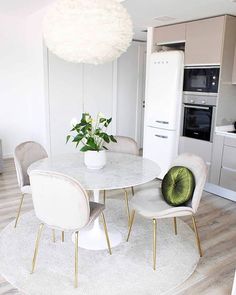 a white table with four chairs and a vase on top of it in the middle of a room