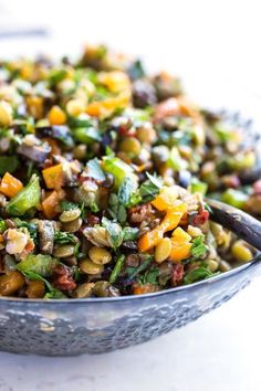 a metal bowl filled with mixed vegetables on top of a white countertop next to a spoon