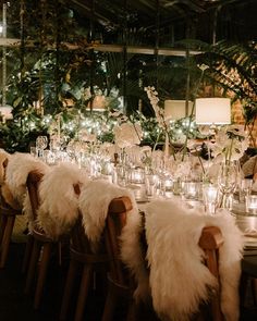 a long table with white fur chairs and candles