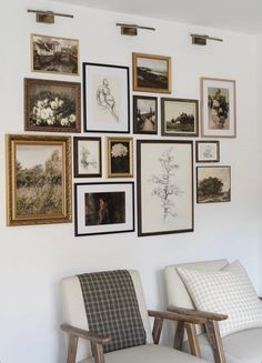 there are many framed pictures on the wall above two chairs and one chair is upholstered