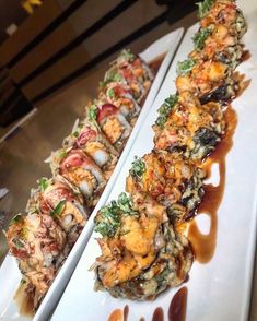 two white plates topped with sushi covered in sauce and garnished with toppings