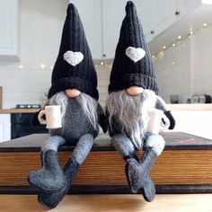 two knitted gnomes sitting on top of a book in the middle of a kitchen