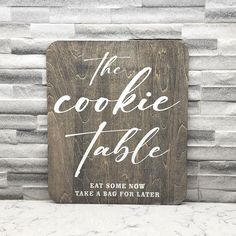 a wooden sign that says the cookie table with white lettering on it, against a brick wall