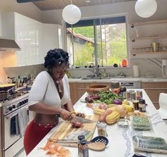 a woman standing at a kitchen counter cutting vegetables on a cutting board with a knife