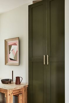 a wooden table sitting next to a green cabinet in a room with paintings on the wall