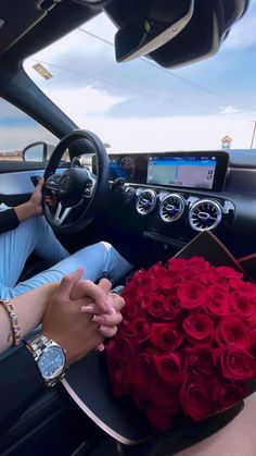 a man sitting in the driver's seat of a car next to a bouquet of red roses