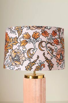 a pink table lamp with an orange and yellow flower print shade on top of it