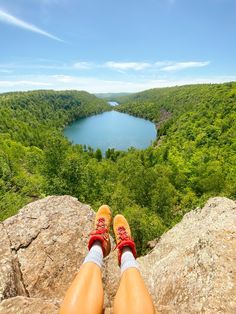 a person's feet with red shoes standing on top of a rock overlooking a lake