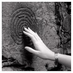 a person's hand reaching out towards a rock with an intricate design on it