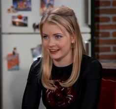 a woman with blonde hair sitting in front of a refrigerator