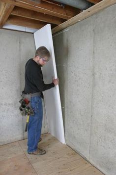 a man standing next to a wall in a room with unfinished walls and wood flooring