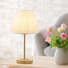 a vase with pink roses sitting on a table next to a white chair and lamp