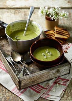 two bowls of soup are sitting on a tray with spoons and crackers next to them