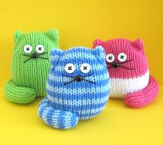 three knitted cats sitting next to each other on a yellow surface with one cat looking at the camera