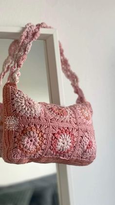 a pink crocheted purse hanging from a hook in front of a white wall