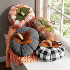 three pumpkins sitting on top of a window sill next to a plaid pillow