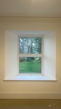 an empty room with white walls and a window in the center that looks out onto a grassy field