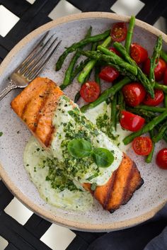 a plate with salmon, asparagus and tomatoes on it next to a fork