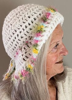 an older woman wearing a white crocheted hat with flowers on the brim