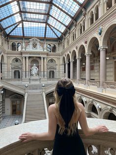 a woman in a black dress is looking down at the staircases and glass ceiling