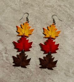 two pairs of maple leaf earrings hanging from hooks on a marble surface in autumn colors