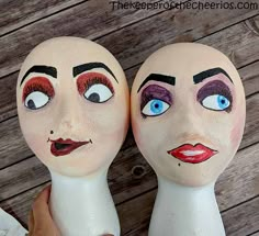 two white mannequin heads with blue eyes and red lips, one is holding the other's head