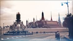 a large building with many spires in the background and people walking by on the sidewalk