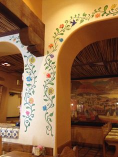 the interior of a restaurant with painted flowers on the wall and wooden tables in front of it