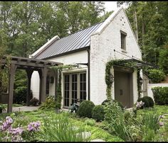 a white brick house surrounded by greenery and flowers