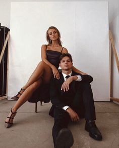 a man sitting next to a woman in a black dress and high heels on the floor