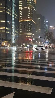 a city street at night with lots of lights and buildings in the background on a rainy day