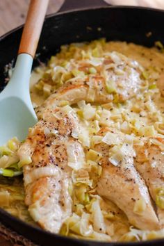 a skillet filled with chicken and cabbage covered in gravy next to a wooden spoon