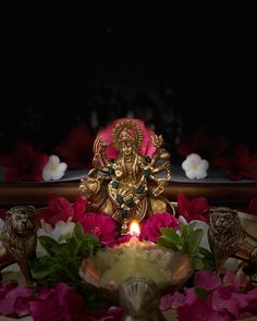 a small statue sitting on top of a table next to some pink flowers and candles