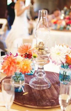 the table is set with vases and flowers on it, along with wine glasses