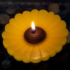 a yellow candle with a brown center sitting on some rocks